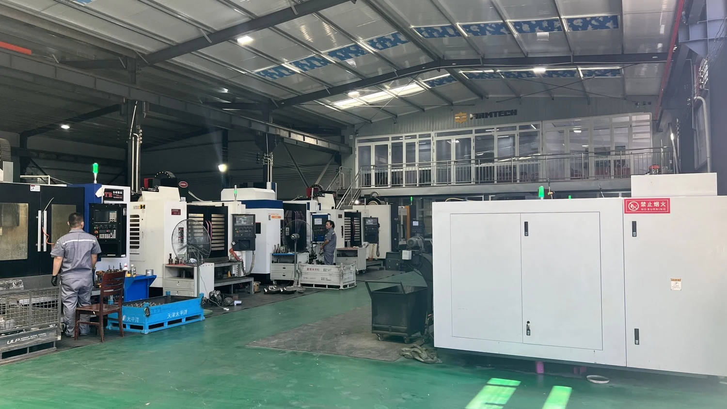 Hai công nhân vận hành máy đang làm việc trong xưởng, với biển FIRMTECH nguyên bản hiện rõ